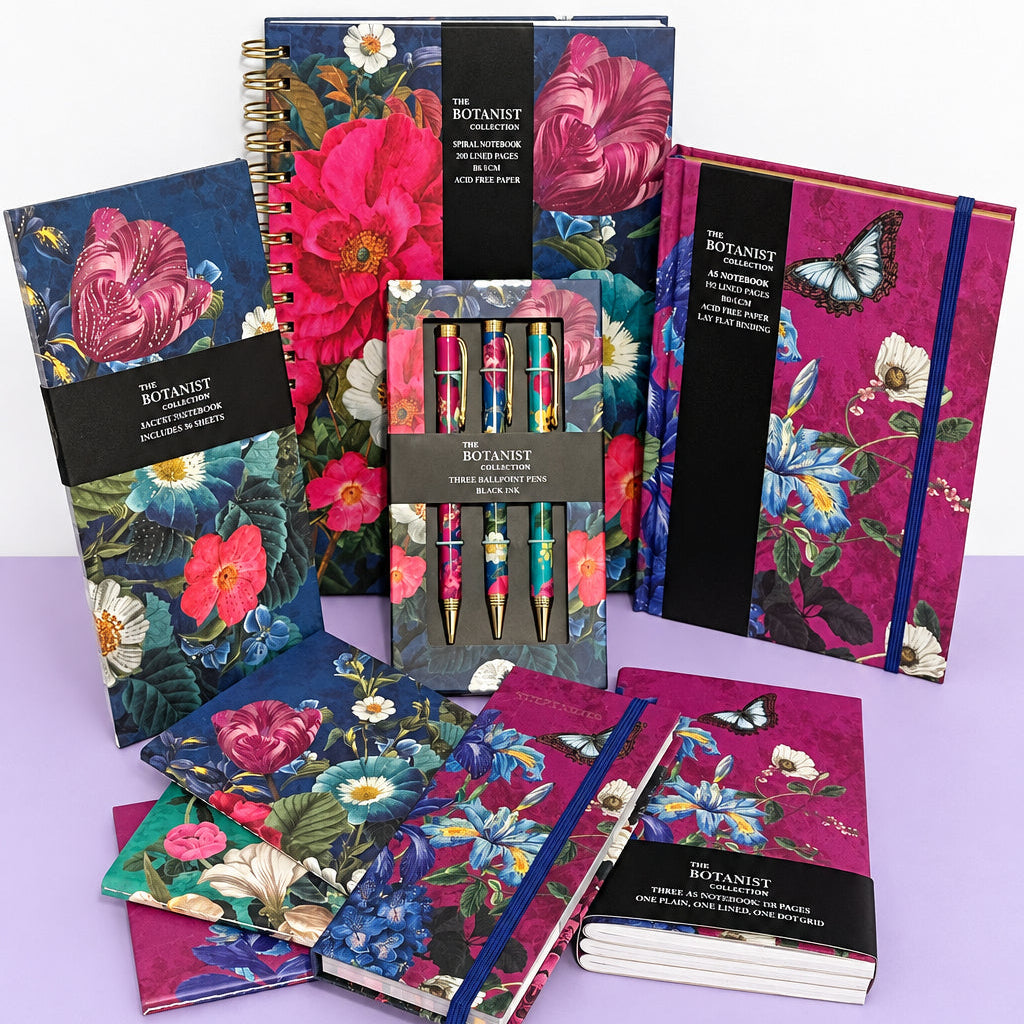A collection of floral and butterfly-themed stationery items, including notebooks, a pen set, and a notebook set, displayed on a white table against a plain wall.