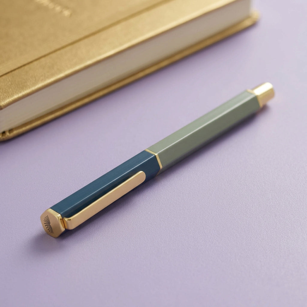 Pen with green and blue design on a lilac desk with a gold journal in the background