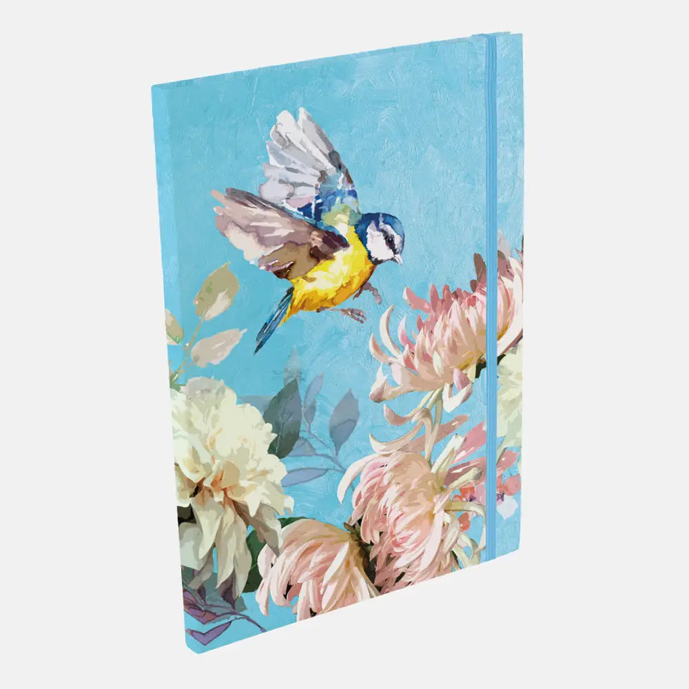 A hardcover notebook with a vibrant blue cover featuring a painted bluebird in flight and pink and cream flowers, shown at an angle on a light gray background.