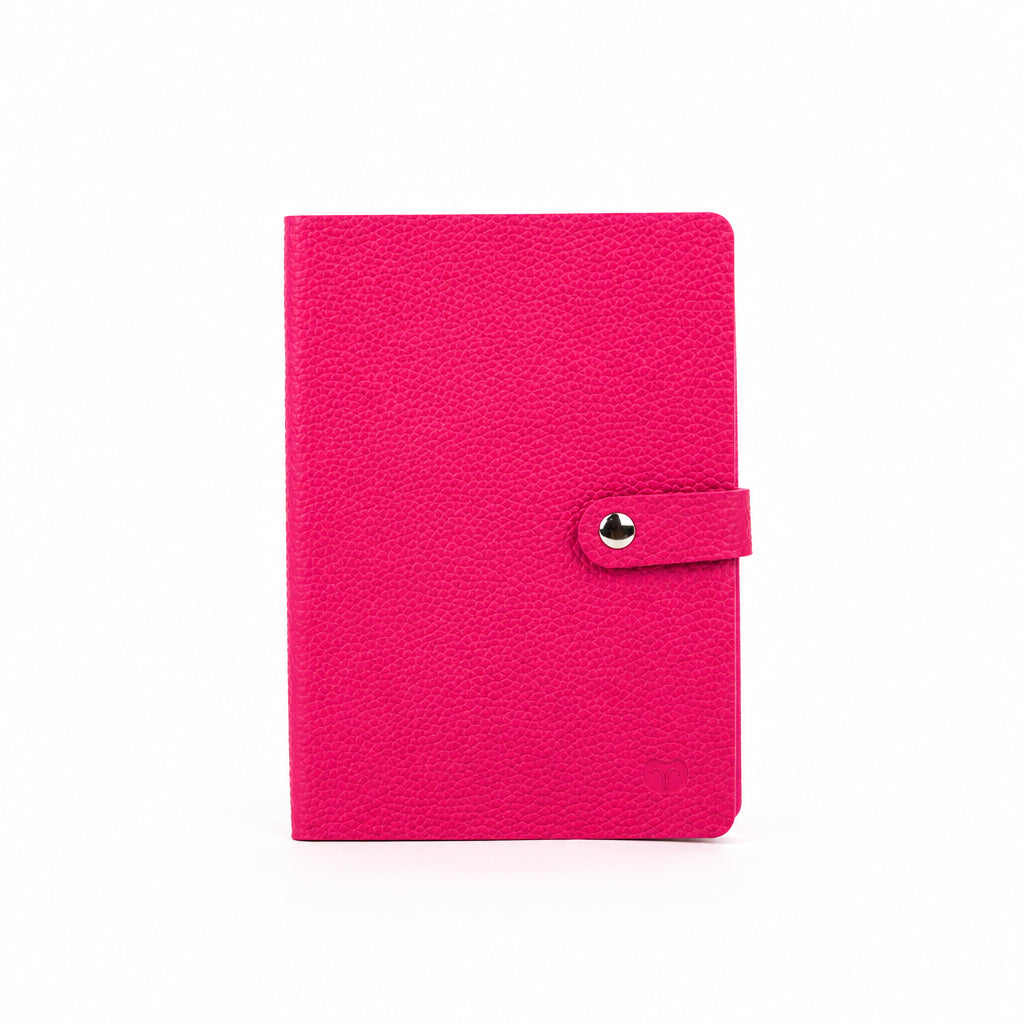 Magenta A5 notebook with a textured cover and matching strap with a silver-tone snap-button closure, on a white background