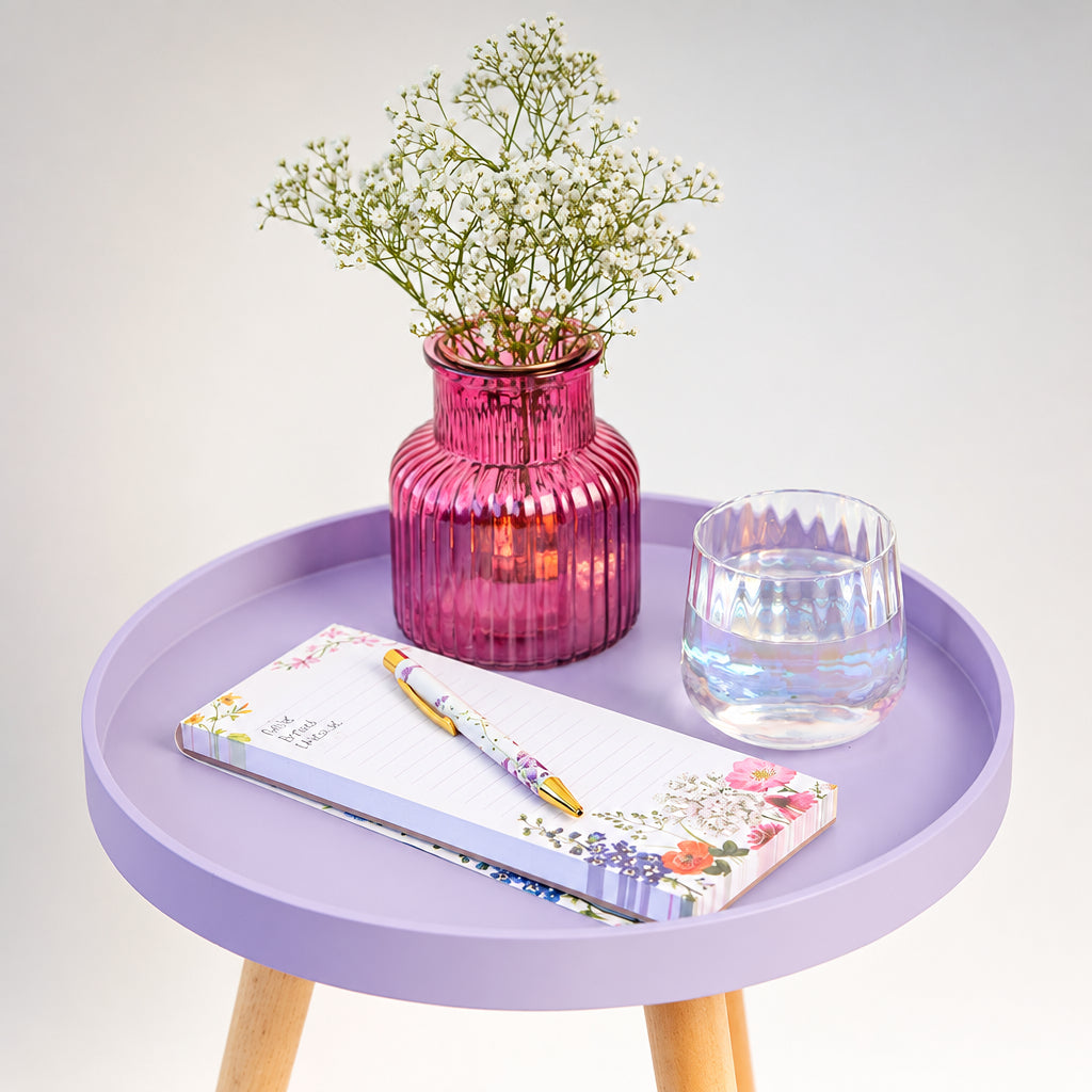 Small round table with a pink vase, glass of water, and notebook on a light gray background