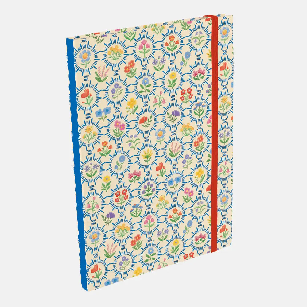 A hardcover notebook with a cream-colored cover decorated with a dense, colorful floral and botanical pattern. The notebook features a bright blue spine and is secured with a red elastic closure band, shown at an angle on a light gray background.