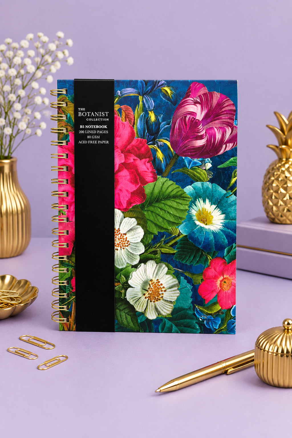 A spiral-bound notebook titled 'The Botanist' from The Botanist Collection, featuring a vibrant floral cover illustration with pink, blue, and white flowers on a dark background, with a black spine band.