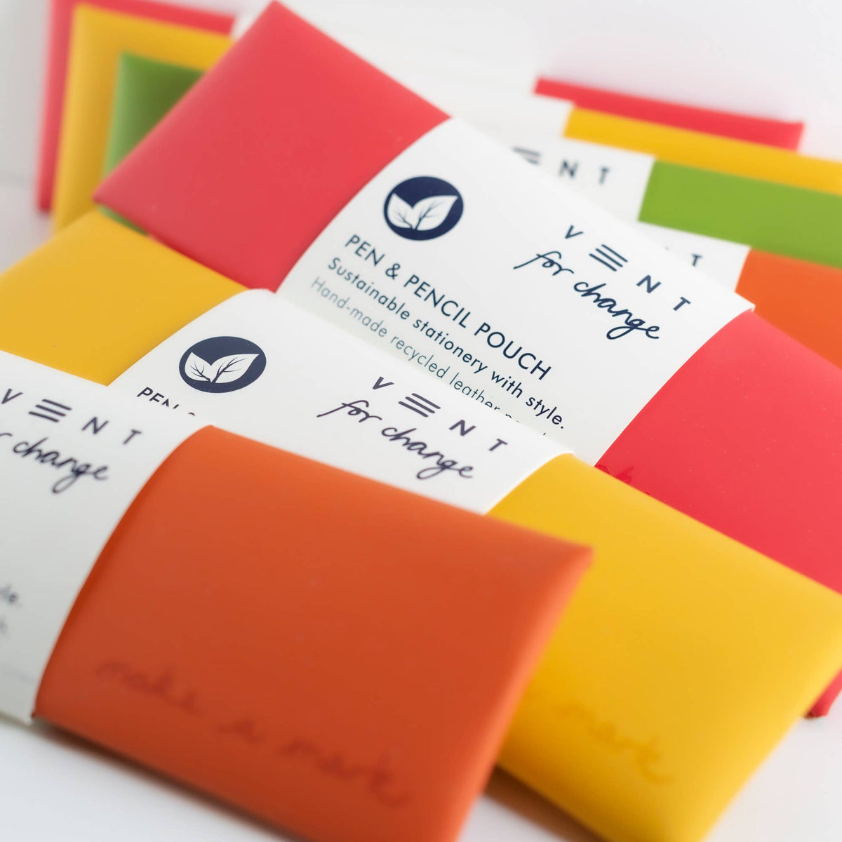 Yellow recycled leather pencil pouch alongside orange and red pencil pouches with their paper sleeves.