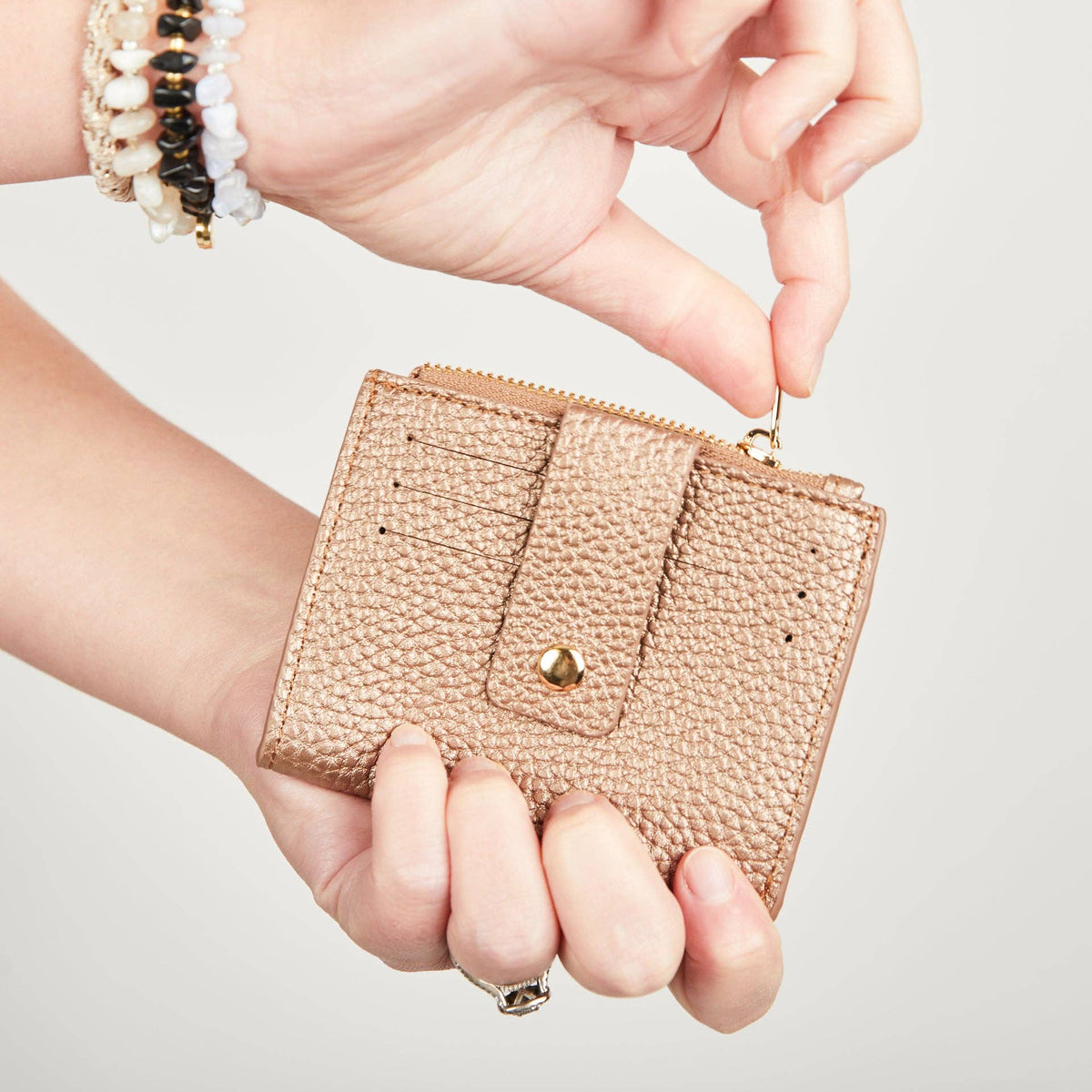 Hands holding a rose gold Pearl Duo purse and demonstrating its gold-tone zip pull.