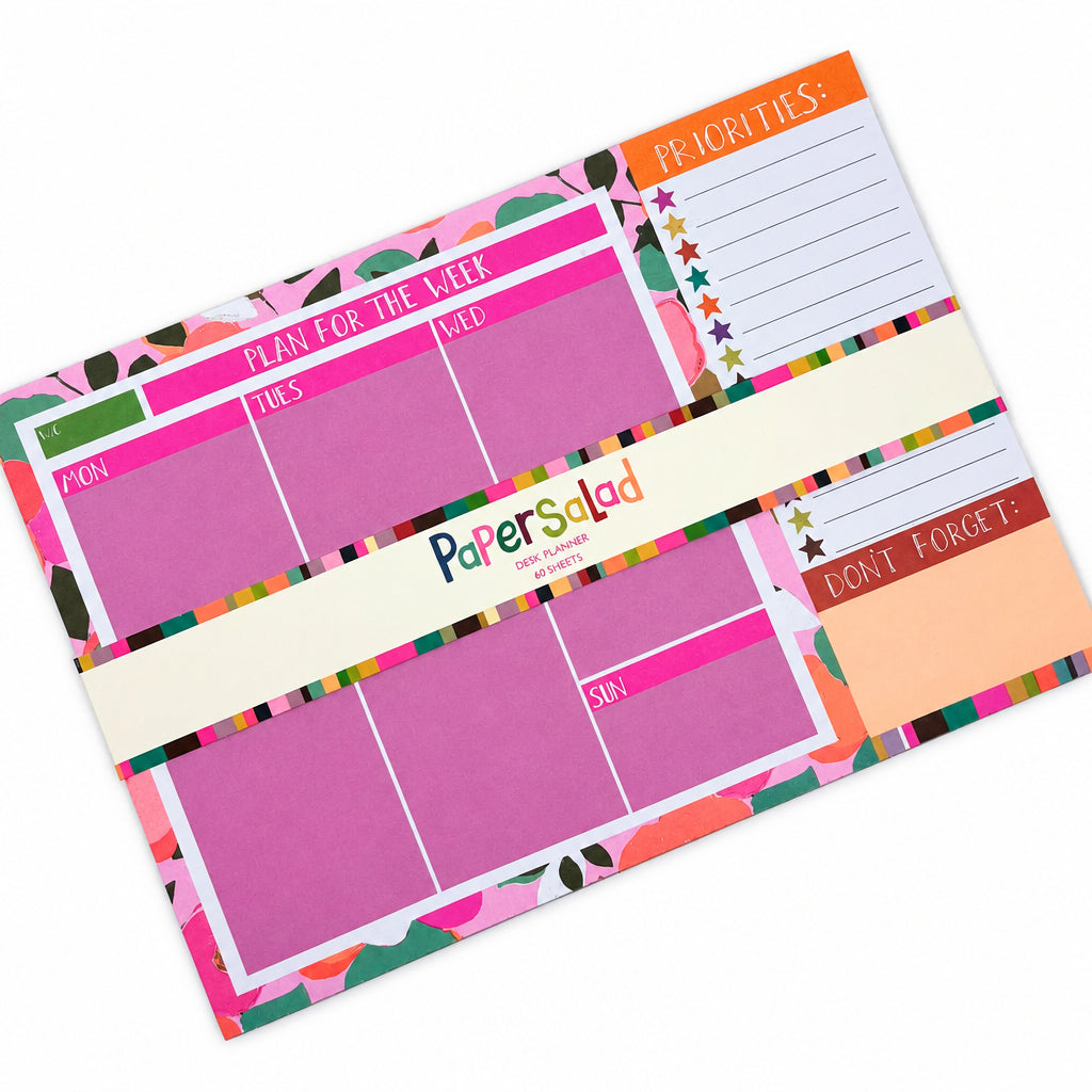 Weekly planner pad on a light grey background, featuring pink, orange and white sections with colourful patterned borders and a central white paper band.