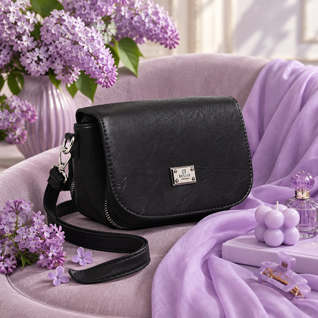 Black crossbody bag on a lilac chair beside purple flowers.