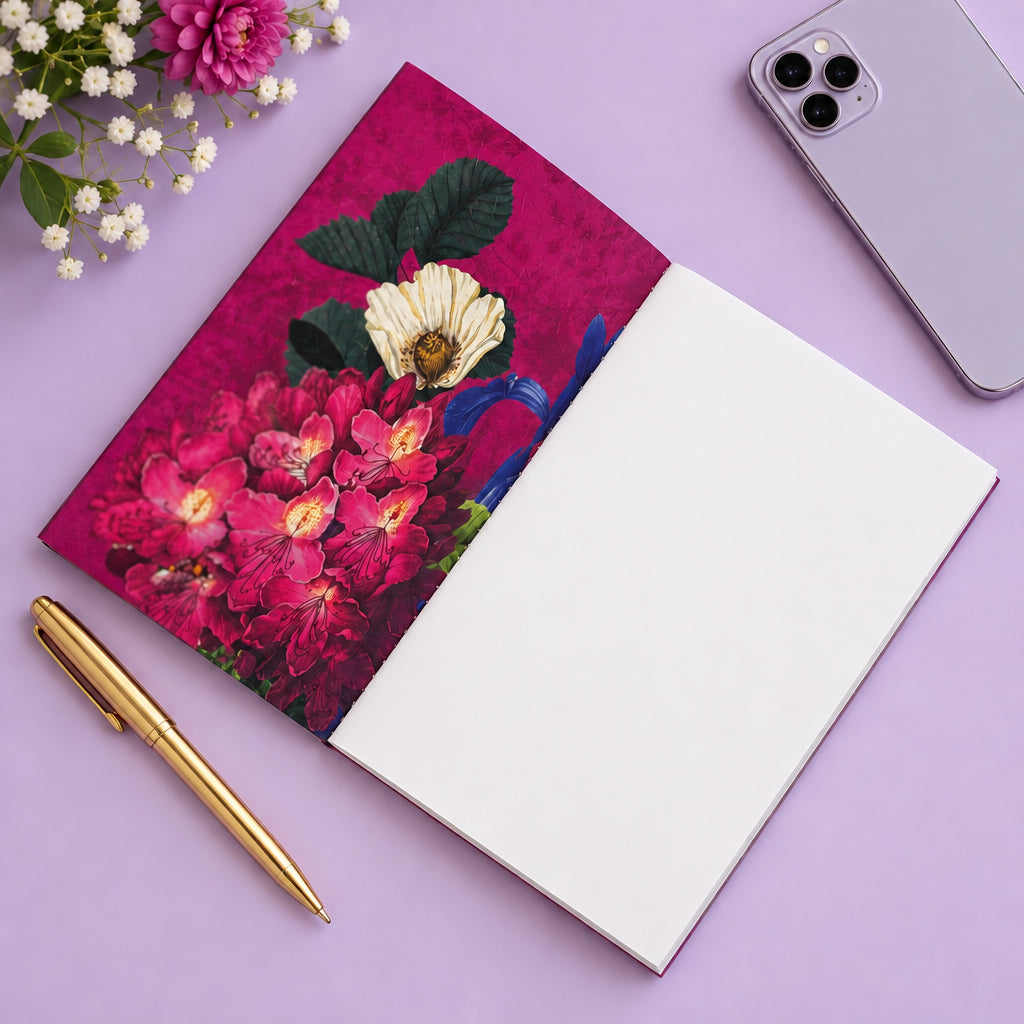 Open Botanist Collection A6 notebook showing a magenta floral inside cover and a blank white page, beside a gold-tone pen and lilac phone on a lilac surface.