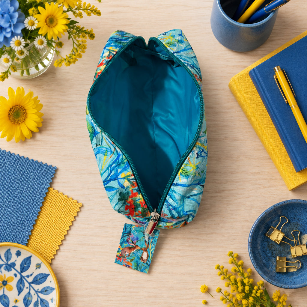  Kissing Hares open pncil case on blue and green tropical floral pattern exterior and a solid teal interior, shown on a light gray surface