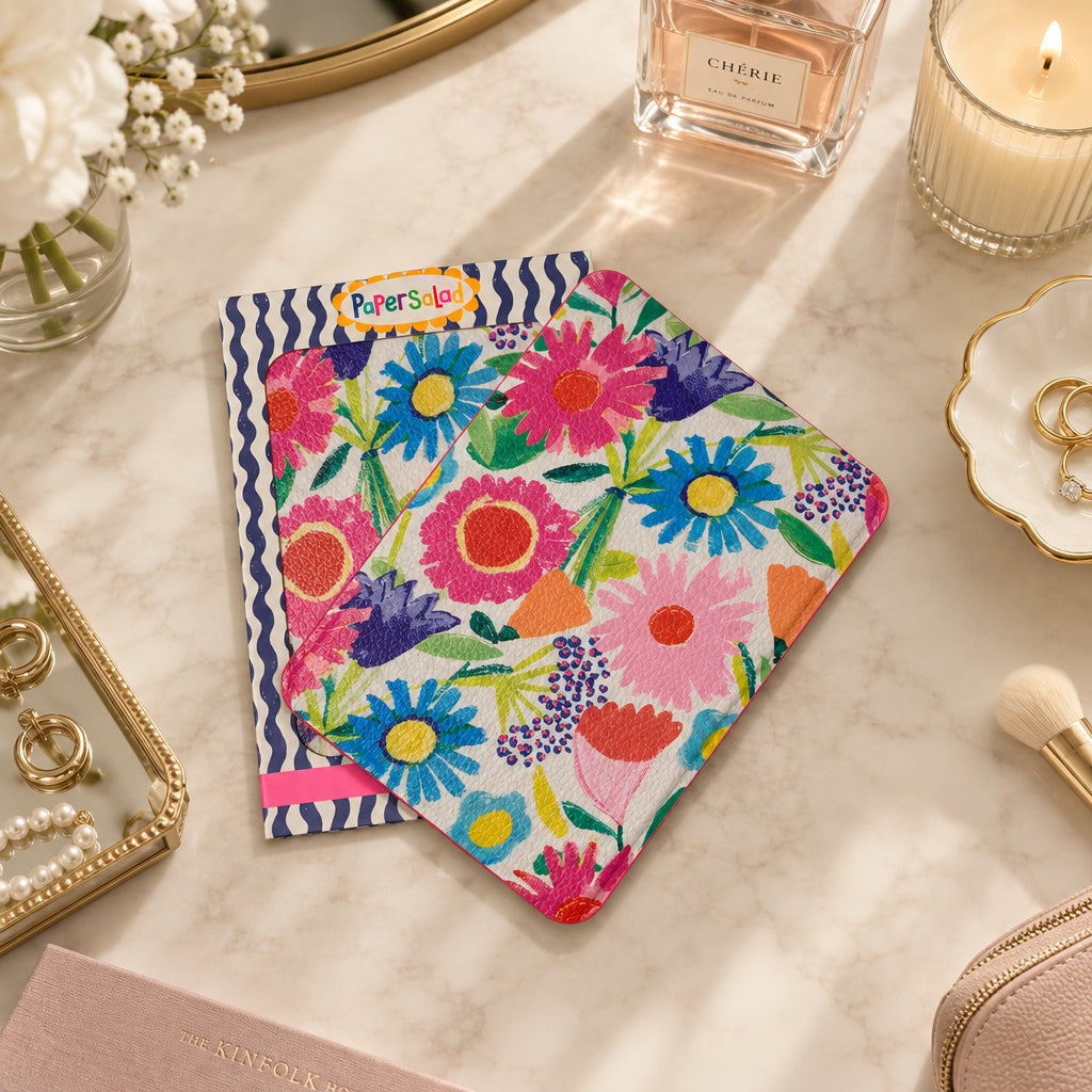 Floral-patterned travel mirror pouch with a colourful daisy print, placed on a navy and white striped paper sleeve.