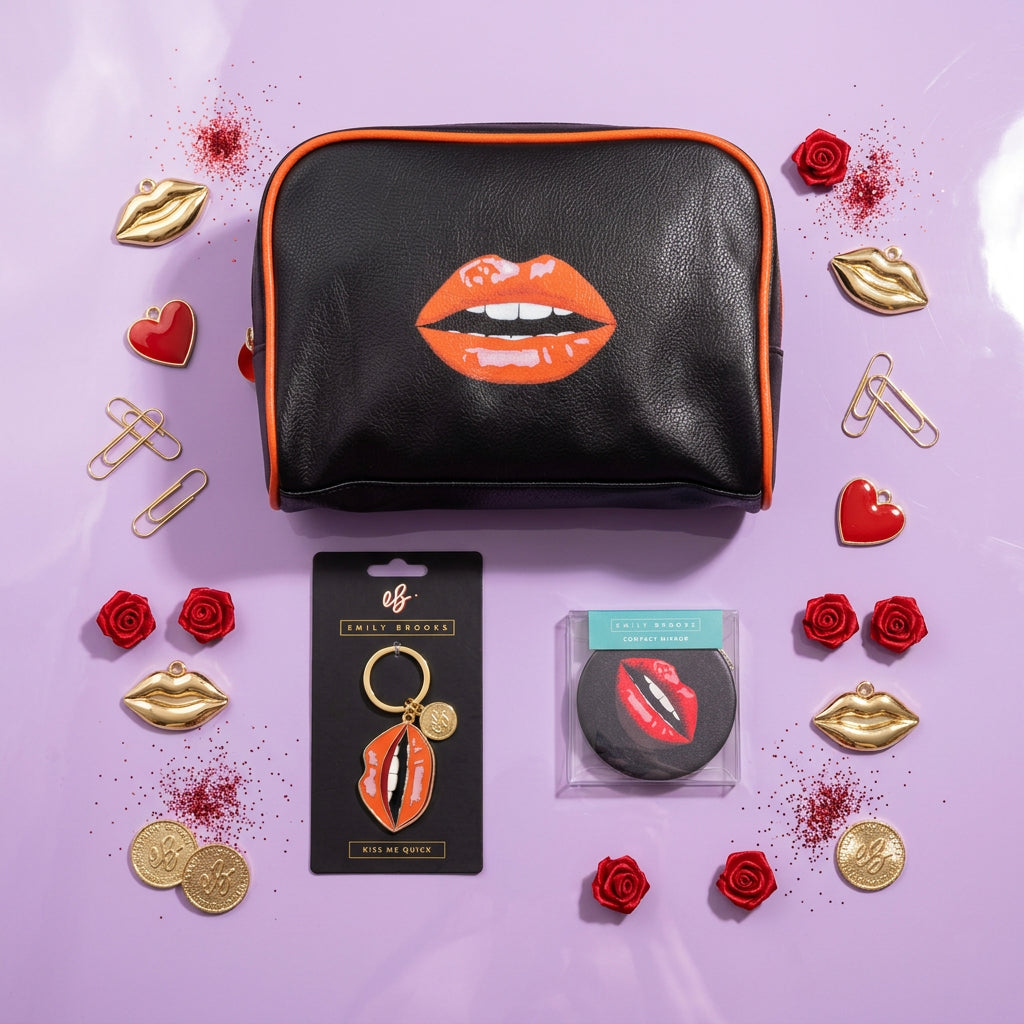 A black faux-leather cosmetic pouch with red trim and a large red lips graphic on the front, shown alongside matching lip-shaped keychain and small round accessory items on a lilac surface.