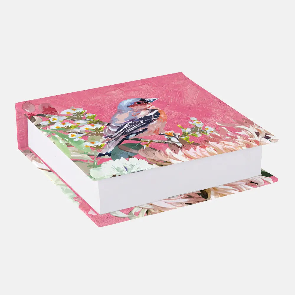 A hardcover notebook or journal with a pink cover decorated with a bluebird perched among white flowers, shown at an angle on a light gray background.