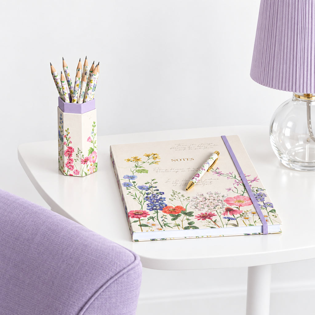 Floral notebook and pencil holder on a wooden table with a lamp in the background