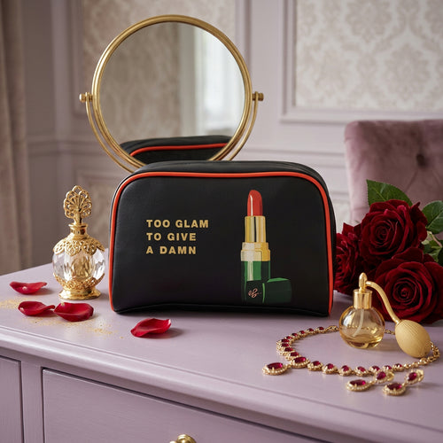 Black cosmetic pouch with red piping, gold text reading 'TOO GLAM TO GIVE A DAMN', and a graphic of a green and red lipstick on a white background.