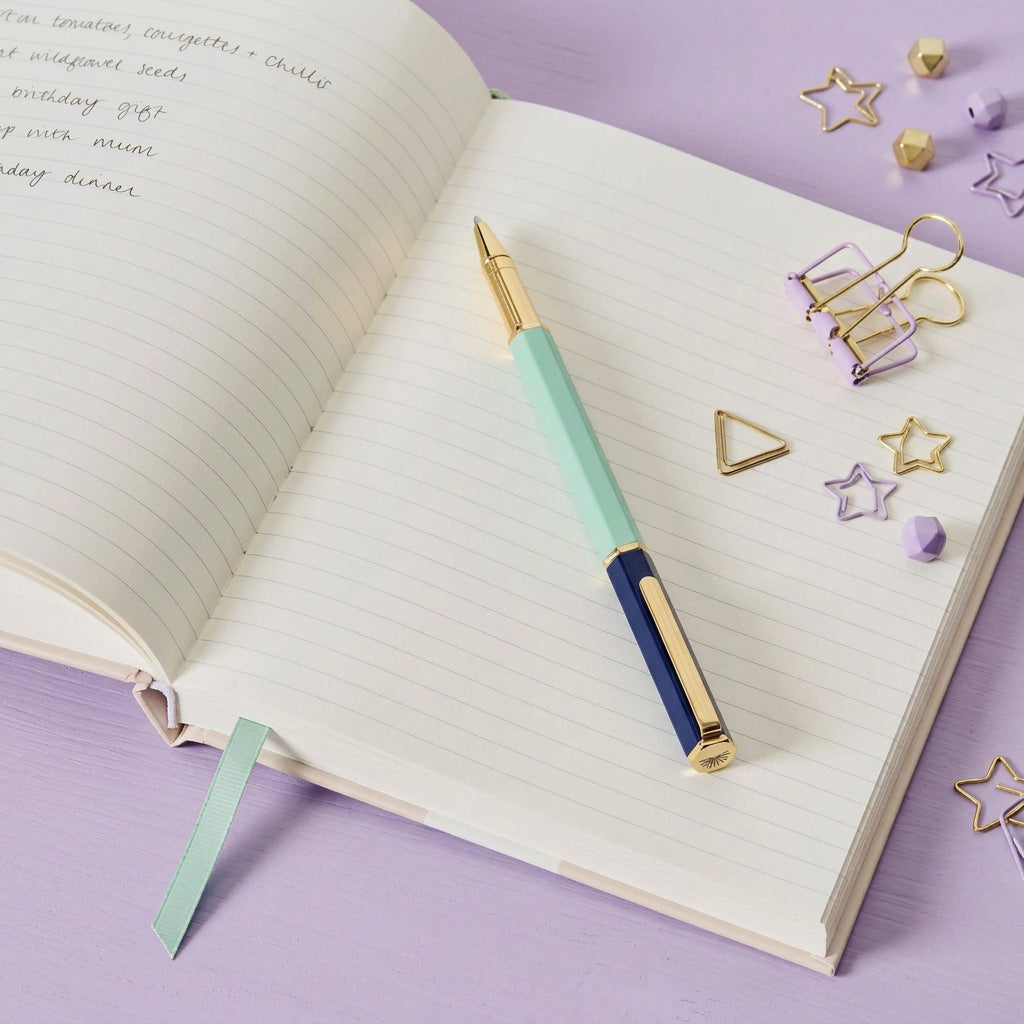 Pen on an open notebook on a lilac desk with lilac and gold clips and 