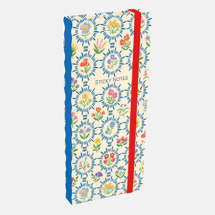 A tall notebook or journal with a cream background and a colorful floral sunburst pattern, featuring a bright red elastic closure band and the words 'STICKY NOTES' printed on the front, shown on a light gray background.