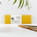 Yellow recycled leather pen and pencil pouch with a paper sleeve, displayed on a desk beside pencils.
