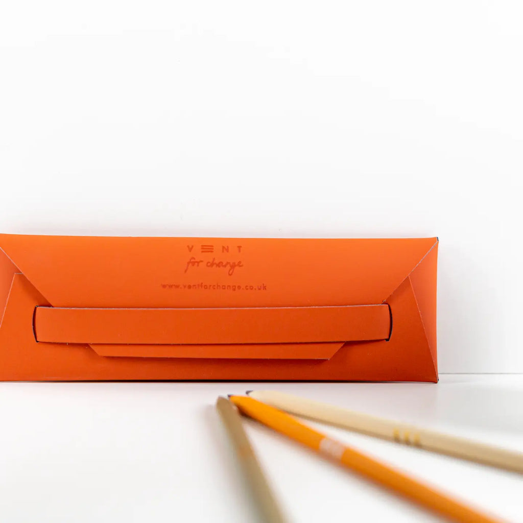 Back of an orange recycled leather pencil case showing its tuck-in closure, displayed beside pencils.